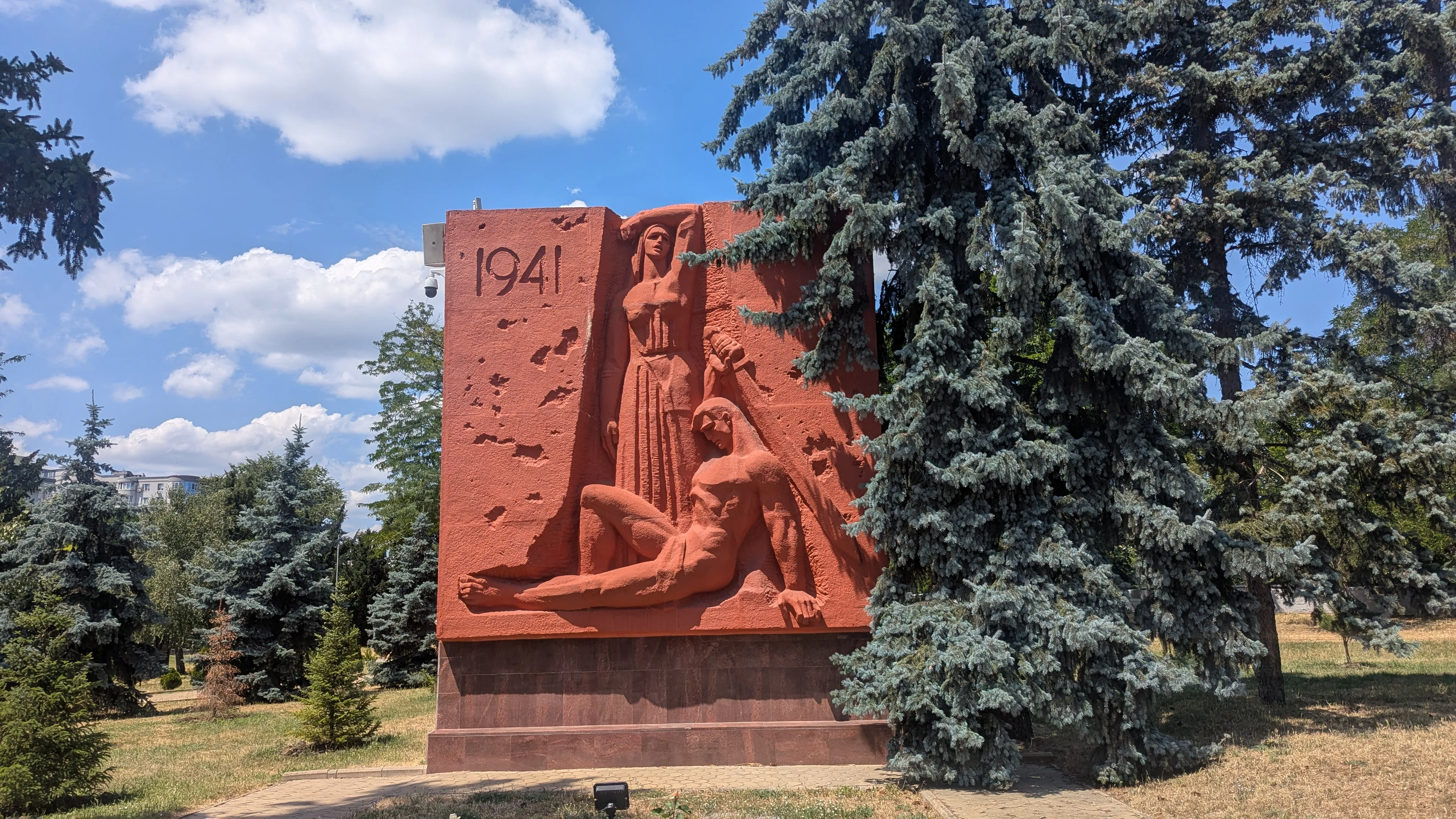 Czerwona brutalistyczna płaskorzeźba mężczyzny z mieczem i rozpaczającej kobiety z datą 1941