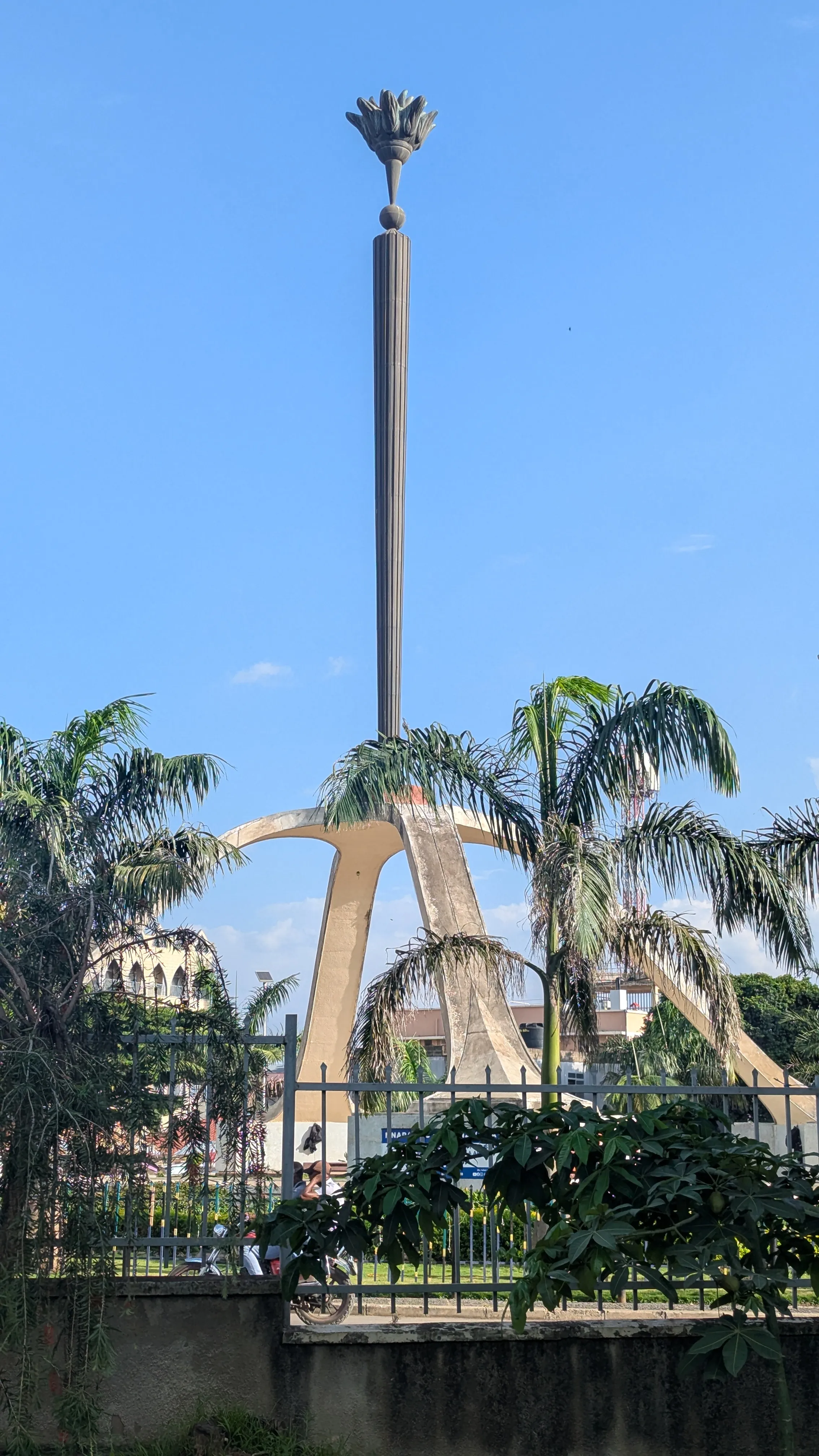 Pomnik w kształcie wyniesionego w górę znicza, otoczony zielenią i
płotem