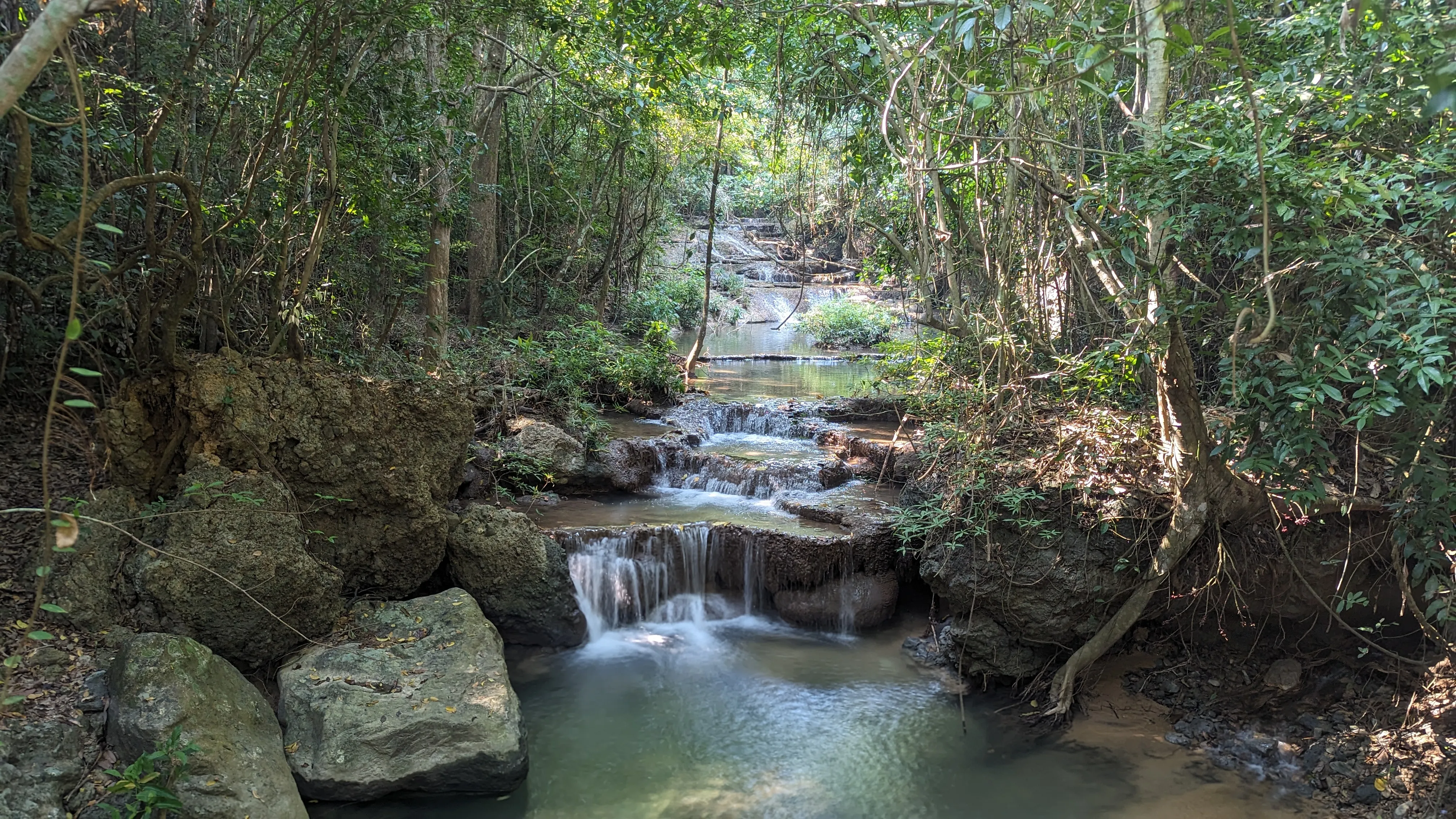 Rzeka spływa kaskadą w dół, wokół gęsty las
tropikalny