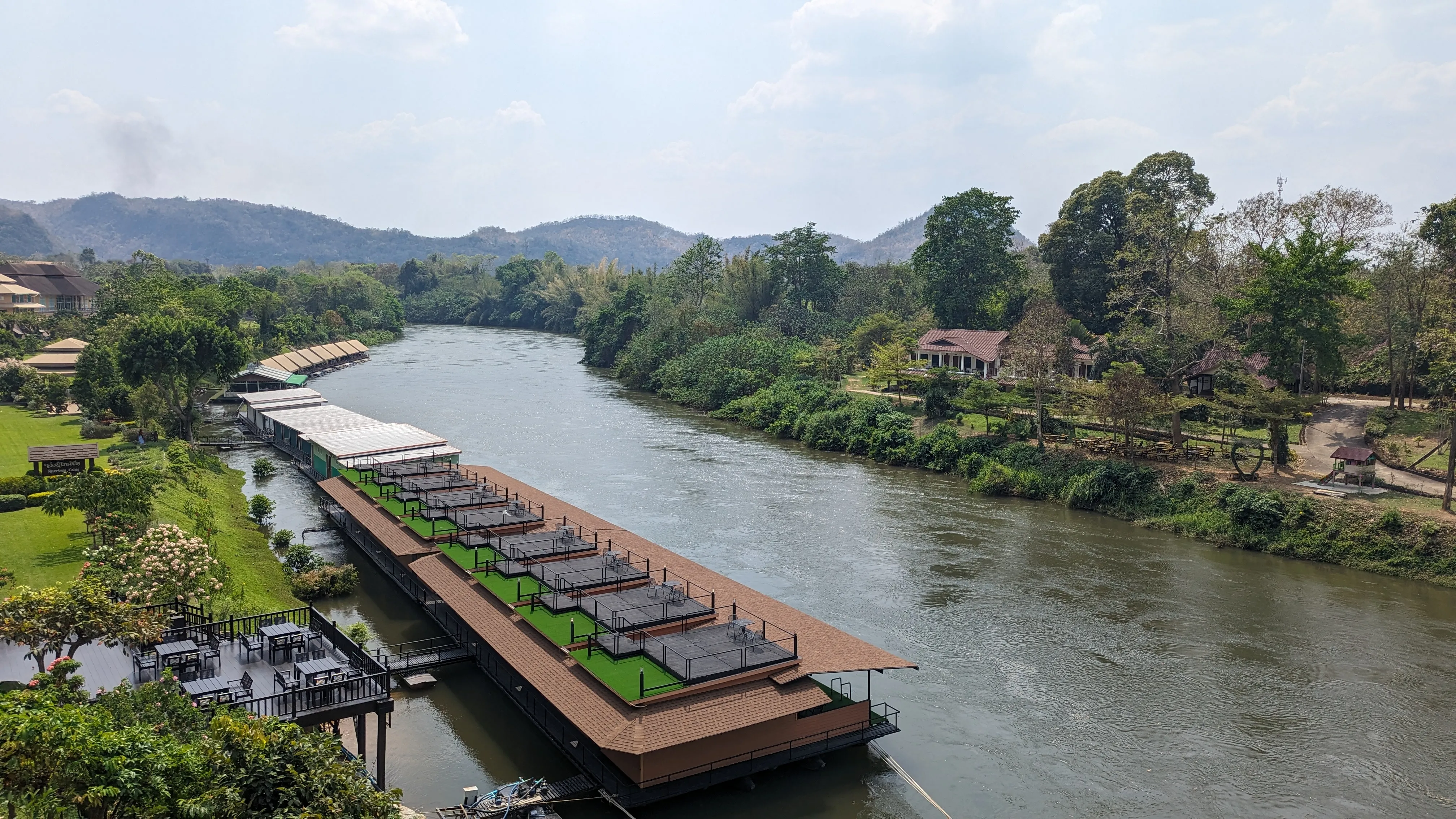 Rzeka, przy brzegu budynki na wodzie, bujna zieleń, góry w
tle