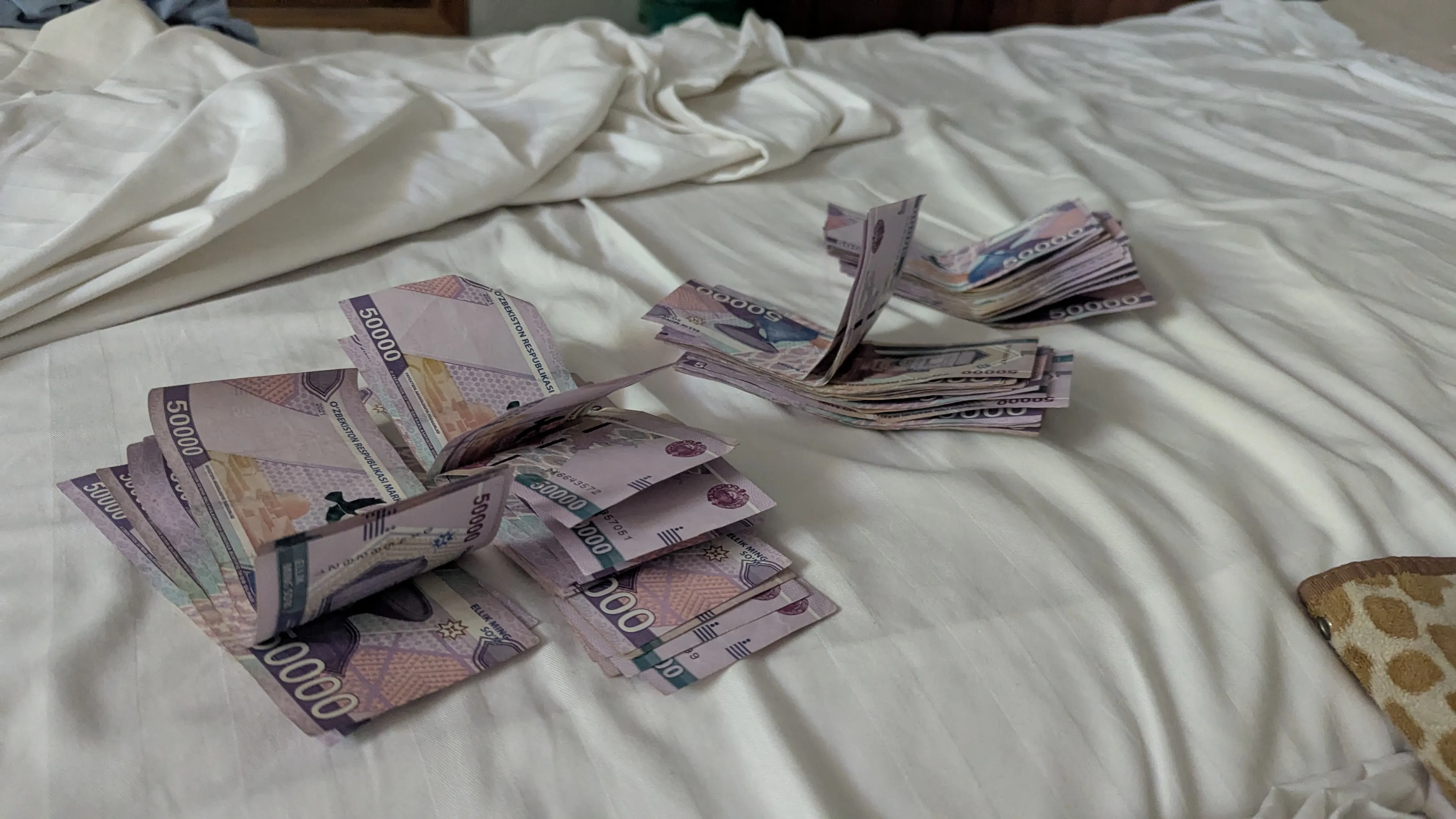 Cztery stosy banknotów o nominale 50000 każdy rozłożone na łóżku