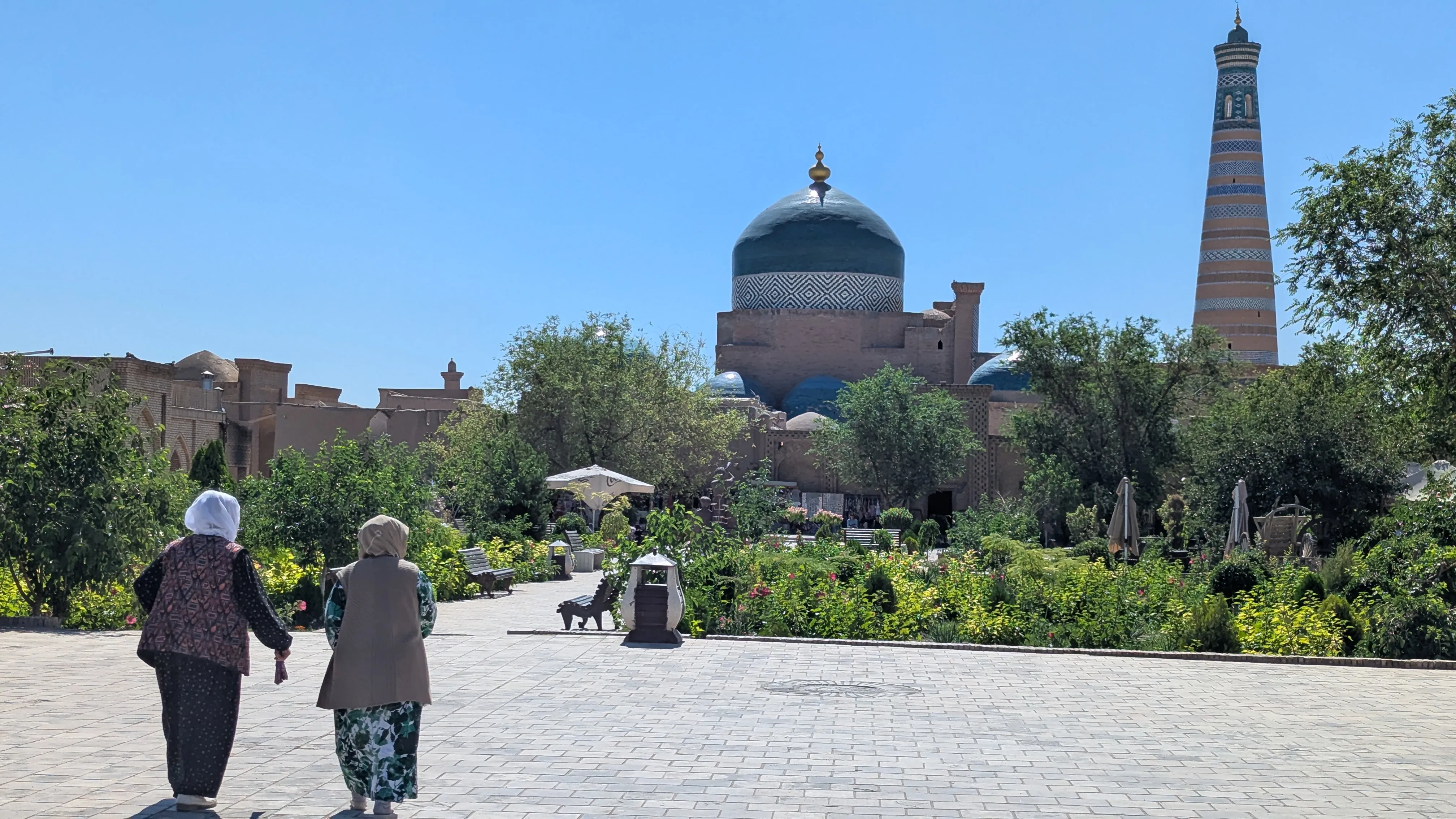 Dwie panie w chustach idą w stronę zielonego skweru, w tle budynek z dużą zieloną kopułą i minaret